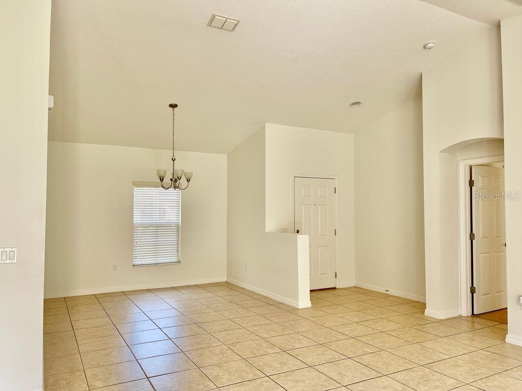 An empty room with beige tile flooring, a chandelier, and a white door — 3856 GULF SHORE CIRCLE, KISSIMMEE, FL
