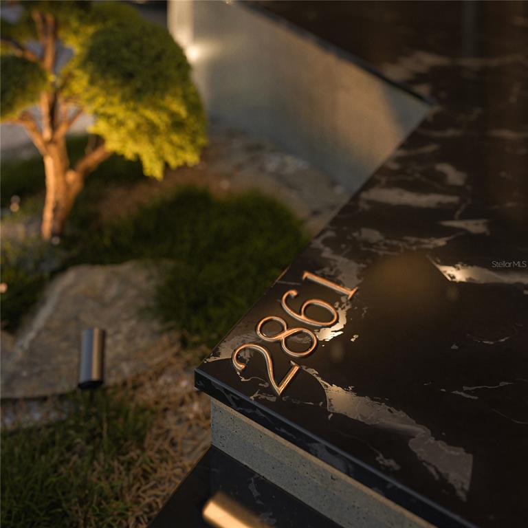 A close-up view of gold house numbers mounted on a black marble-patterned surface — 2861 DON QUIXOTE DRIVE, PUNTA GORDA, FL