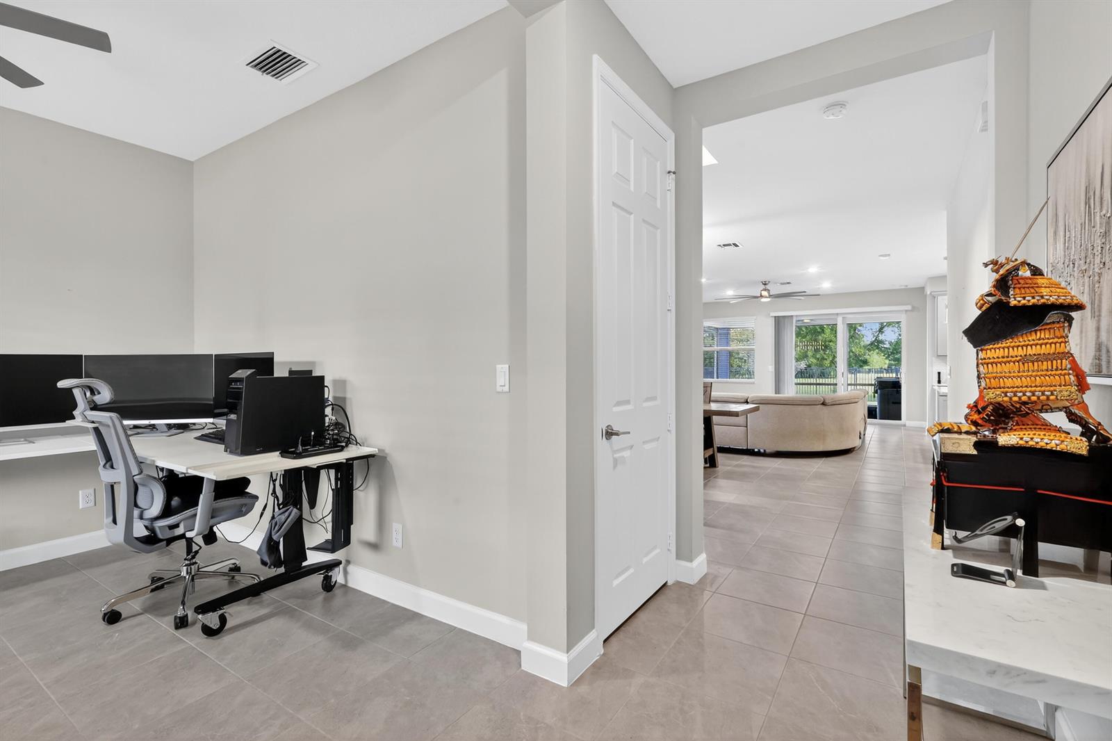 A home office with a desk and computer setup opens into a bright living area — 19753 Tree Stand Terrace, Loxahatchee FL 33470, LOXAHATCHEE, FL