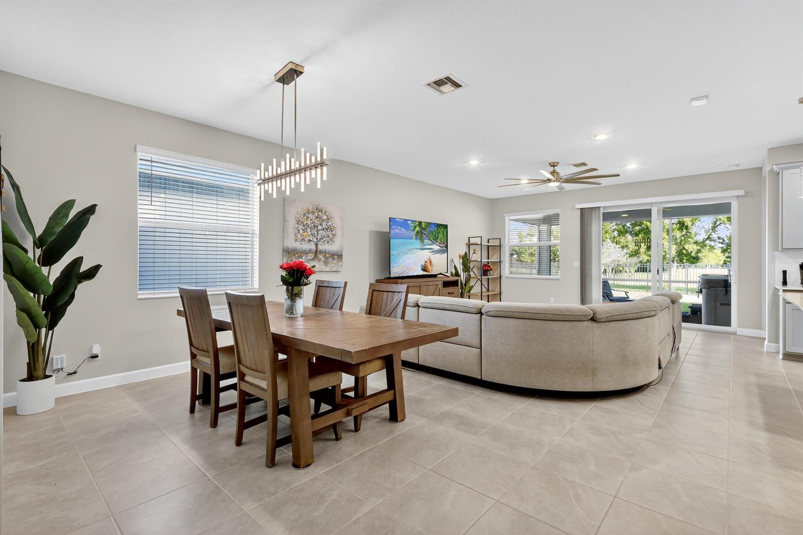 An open-concept living and dining area features tile flooring, a wooden table, and a sectional — 19753 Tree Stand Terrace, Loxahatchee FL 33470, LOXAHATCHEE, FL