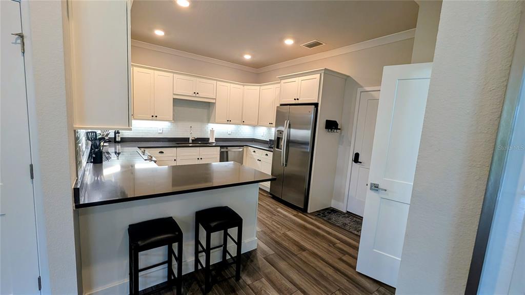 A kitchen features white cabinets, dark countertops, stainless steel appliances, and wood-look flooring — 3062 ISLES WAY, NEW SMYRNA BEACH, FL