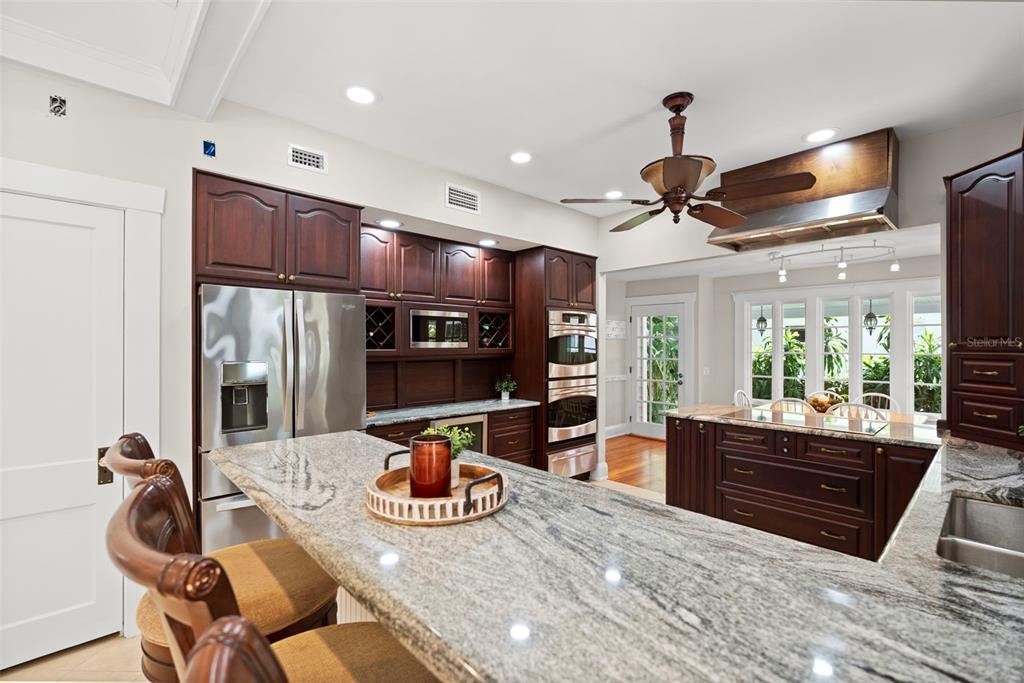 A kitchen features dark wood cabinetry, granite countertops, stainless steel appliances, and a ceiling fan — 703 S EDISON AVENUE, TAMPA, FL