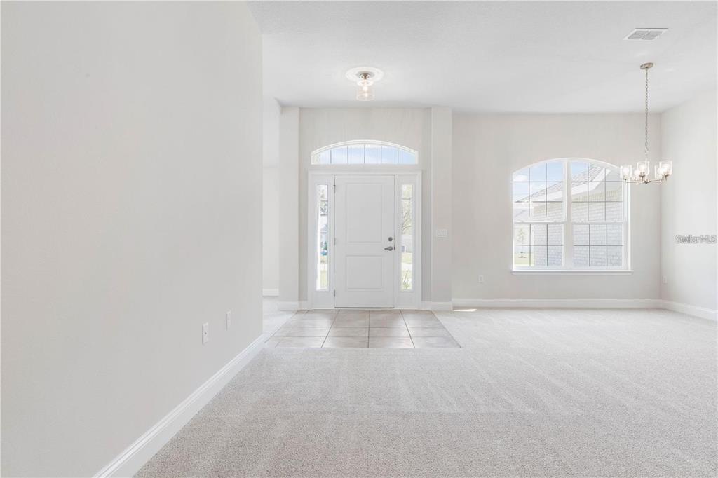 An interior view shows a carpeted living area with a tiled entryway and front door — 74 PRINCETON LANE, PALM COAST, FL