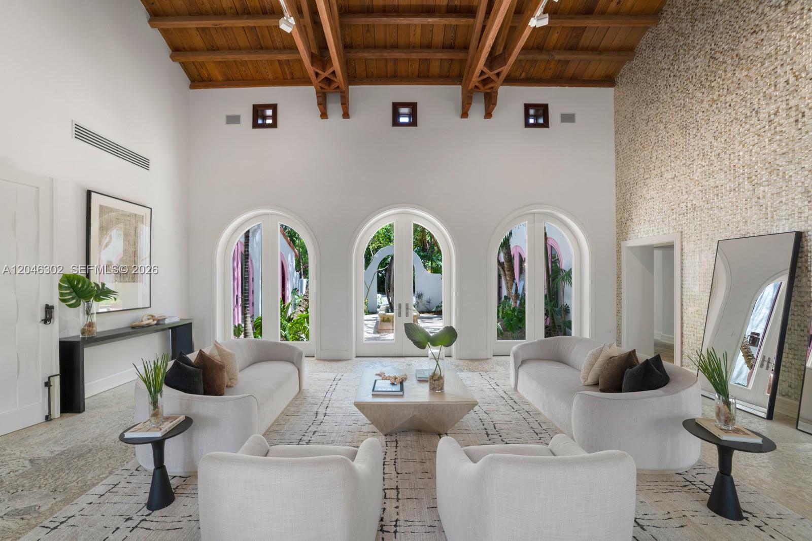 A spacious living room features a vaulted wood ceiling, arched glass doors, and neutral furniture — 16 Palm Ave, Miami Beach FL 33139, MIAMI BEACH, FL