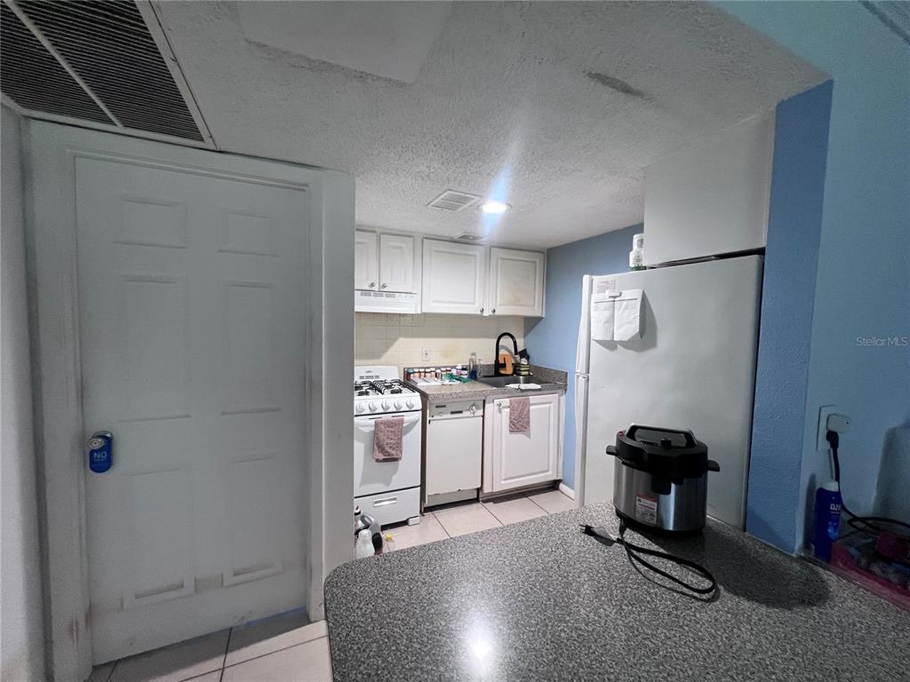 A small kitchen features white cabinets, a white stove, a dishwasher, and a granite countertop — 126 BLUE POINT WAY UNIT 100, ALTAMONTE SPRINGS, FL