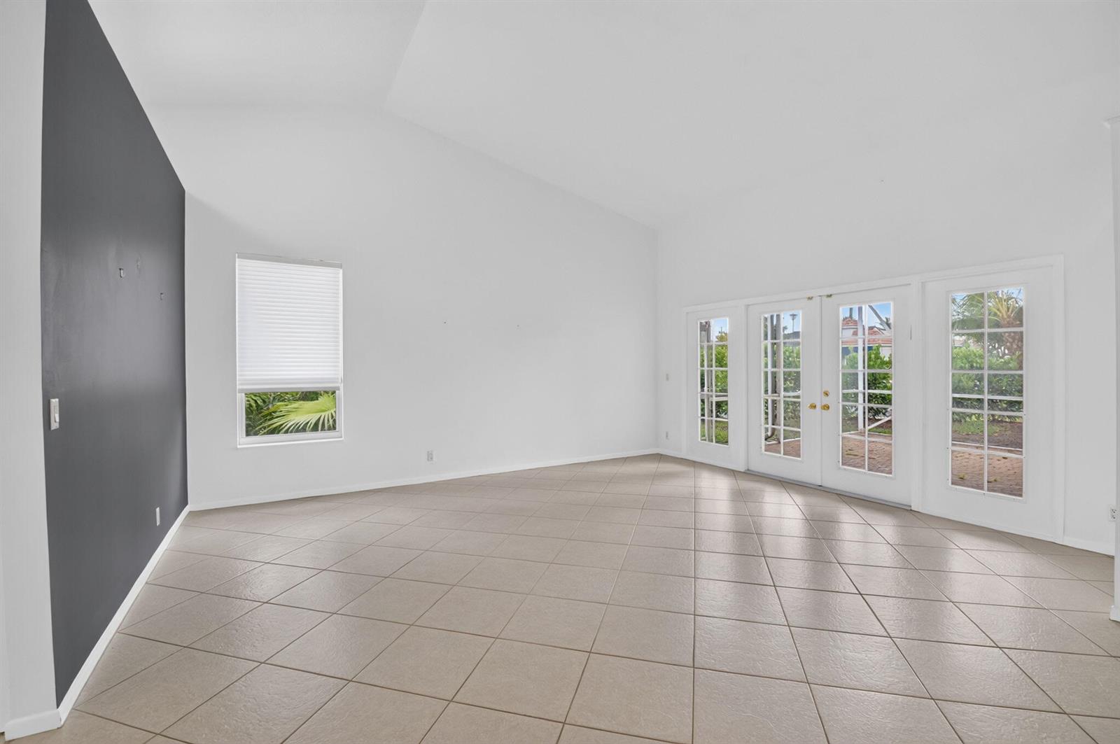 An empty room with a dark accent wall, tile flooring, vaulted ceilings, and glass doors — 23256 Alora Drive, Boca Raton FL 33433, BOCA RATON, FL
