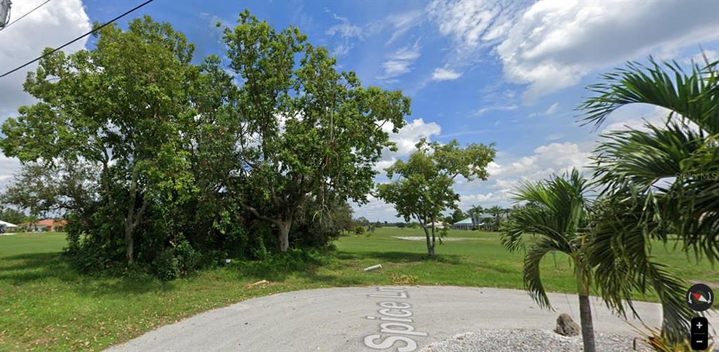 A vacant, grassy lot with mature trees overlooks a golf course from a paved cul-de-sac — 17166 SPICE LANE, PUNTA GORDA, FL