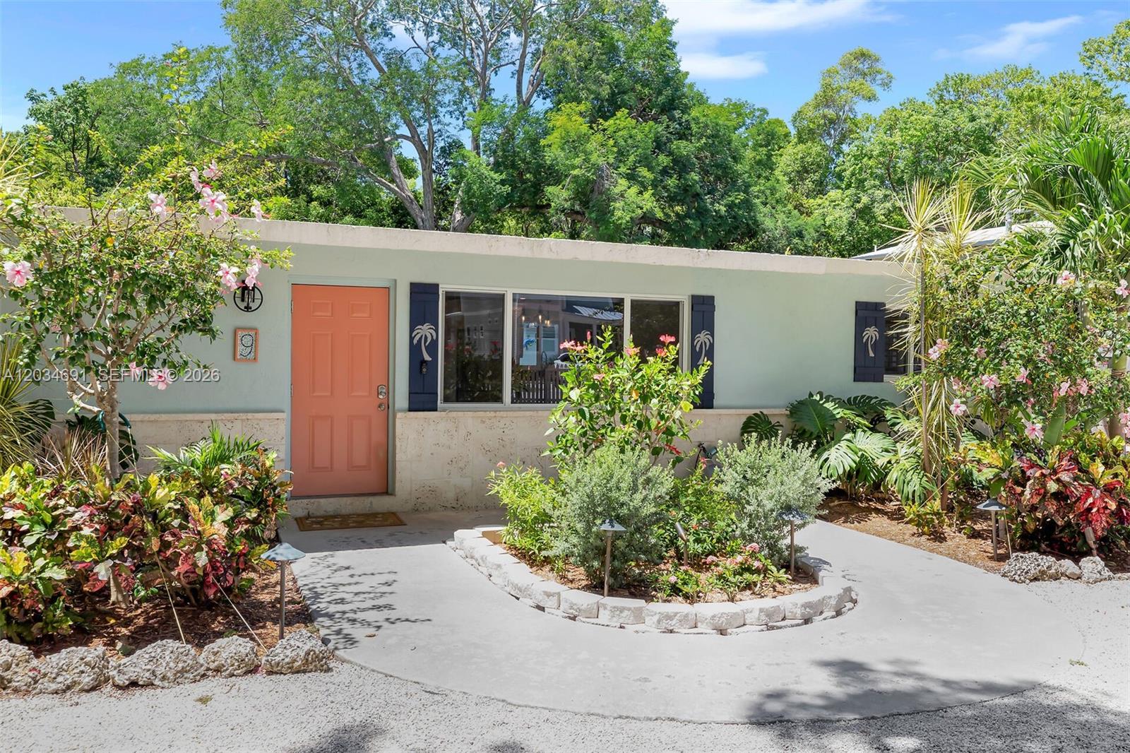 A light green house features a coral door, stone base, and a landscaped front yard — KEY LARGO, FL