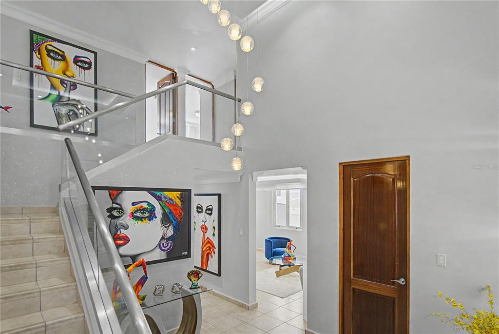 A bright foyer features a glass-railed staircase, modern globe pendant lighting, and colorful wall art — B11 CALLE MAR CARIBE, DORADO, PR