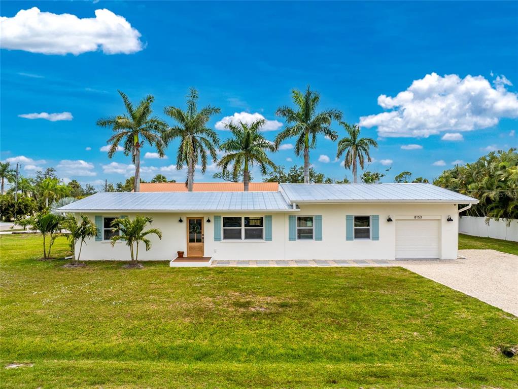 A single-story white house with a metal roof, blue shutters, and palm trees in front — 8153 ROBERT STREET, ENGLEWOOD, FL