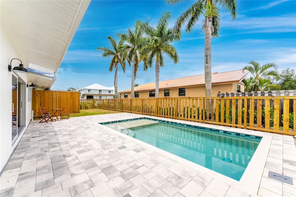 A rectangular swimming pool sits on a paved patio next to a wooden privacy fence — 8153 ROBERT STREET, ENGLEWOOD, FL