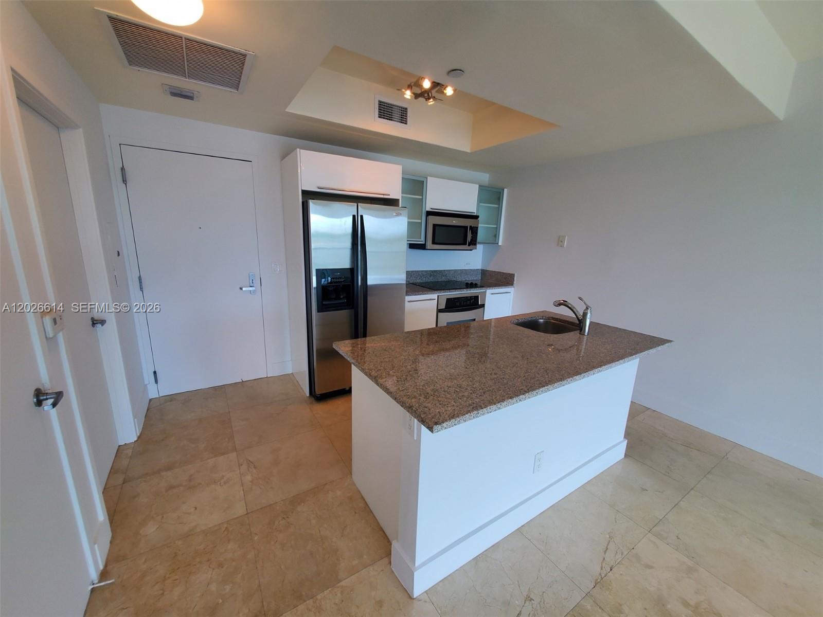 A kitchen features a granite-topped island, stainless steel refrigerator, and light-colored tile flooring — 888 Biscayne Blvd # 311, Miami FL 33132, MIAMI, FL