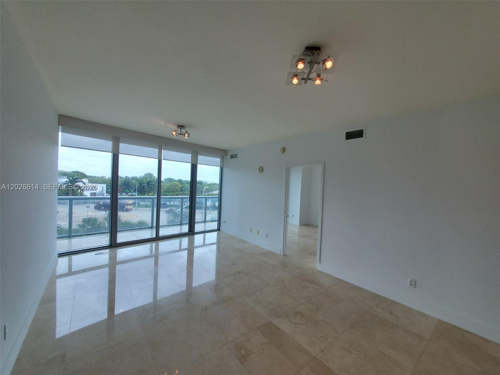 An empty room features light-colored tile floors, white walls, and floor-to-ceiling windows with balcony access — 888 Biscayne Blvd # 311, Miami FL 33132, MIAMI, FL