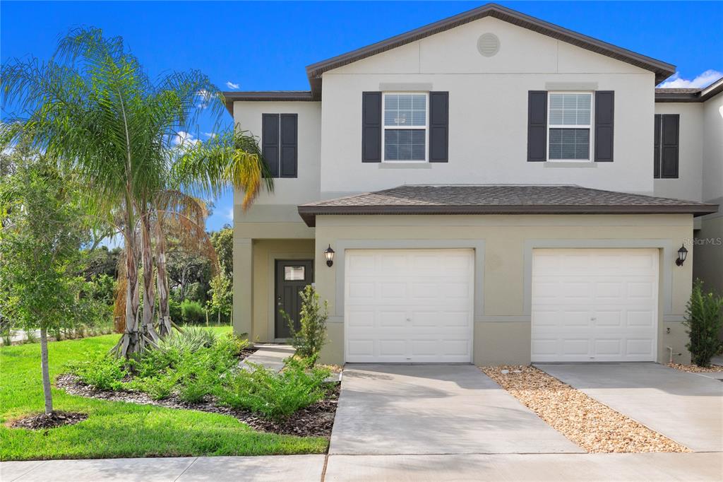 A two-story townhouse with a beige stucco exterior, two garage doors, and a palm tree — 5095 CAPRI HARBOR DRIVE, WIMAUMA, FL