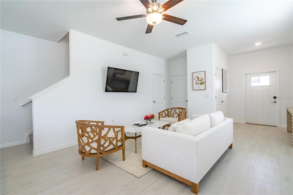 A bright living room features white walls, tile flooring, a sofa, and two wooden chairs — 5095 CAPRI HARBOR DRIVE, WIMAUMA, FL