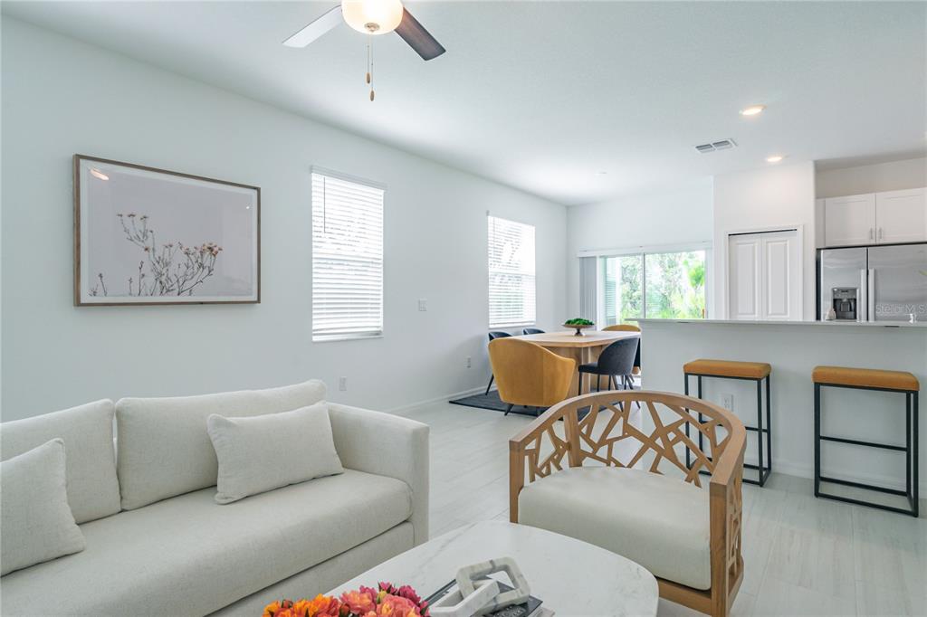 A bright open-concept living and dining area features white walls, tile flooring, and modern furniture — 5095 CAPRI HARBOR DRIVE, WIMAUMA, FL