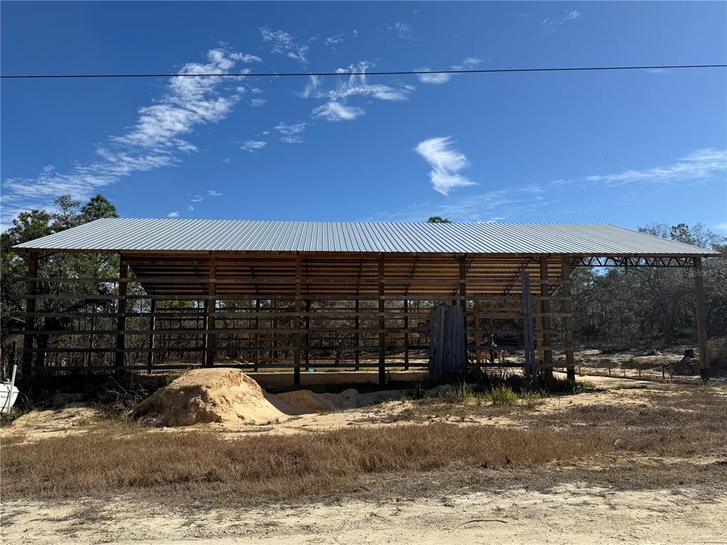 An open-sided pole barn structure stands on a sandy lot under a blue sky — 16386 KAKAWI ROAD, WEEKI WACHEE, FL