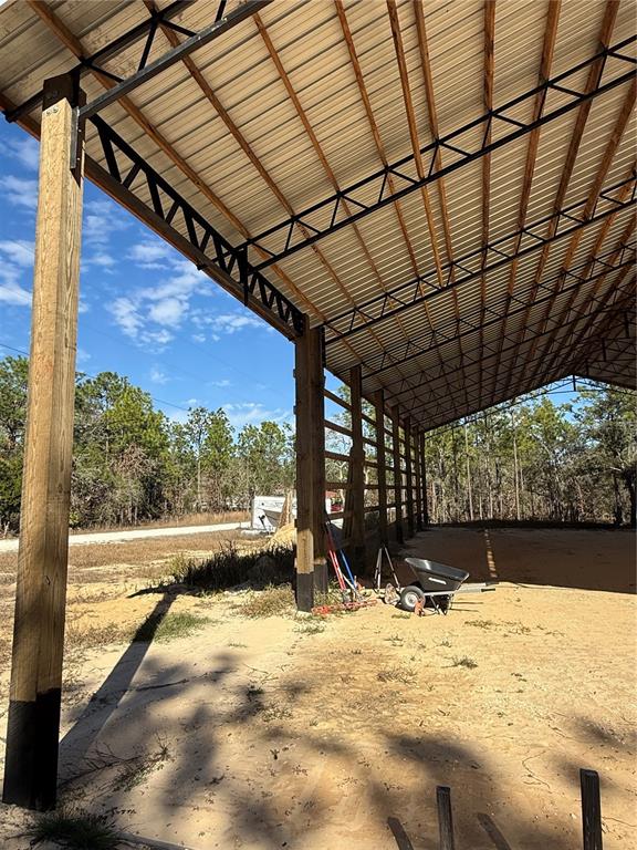 An open-sided metal pole barn structure features a dirt floor with scattered survey stakes — 16386 KAKAWI ROAD, WEEKI WACHEE, FL