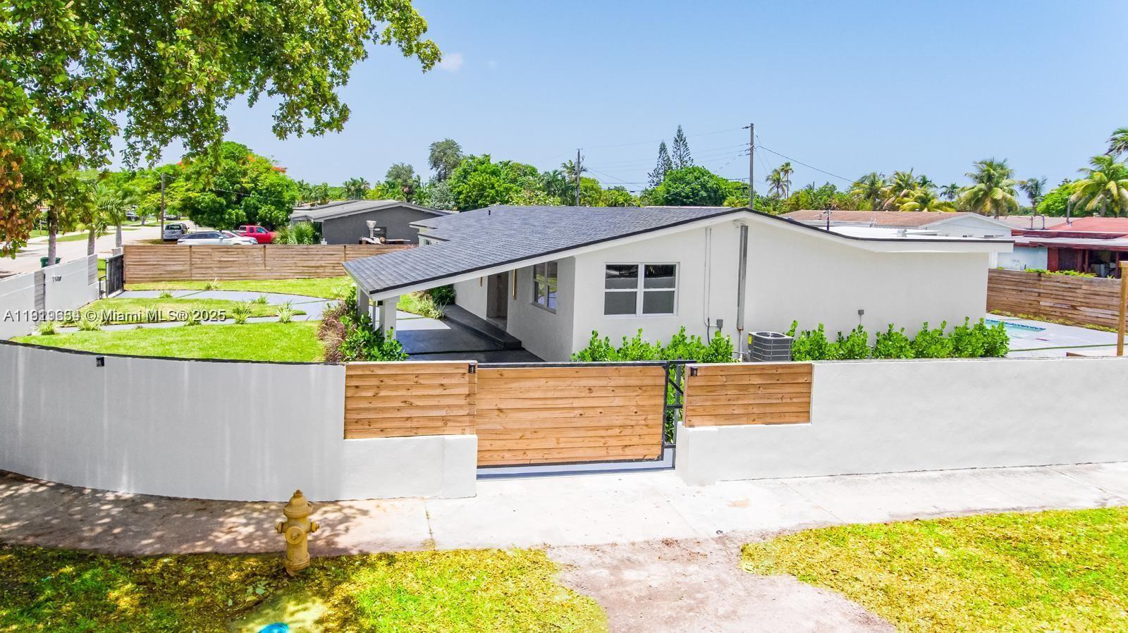 An exterior view of a white single-story house with a wooden gate and fence — 19661 NE 10th Pl, Miami FL 33179, MIAMI, FL