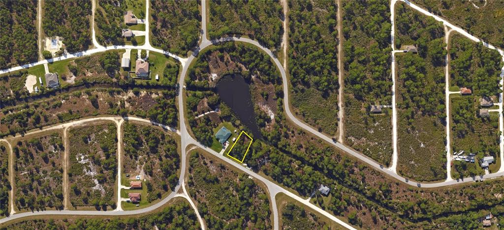 An aerial view shows a vacant lot outlined in yellow next to a pond and house — 27539 MONTE CRISTO BOULEVARD, PUNTA GORDA, FL