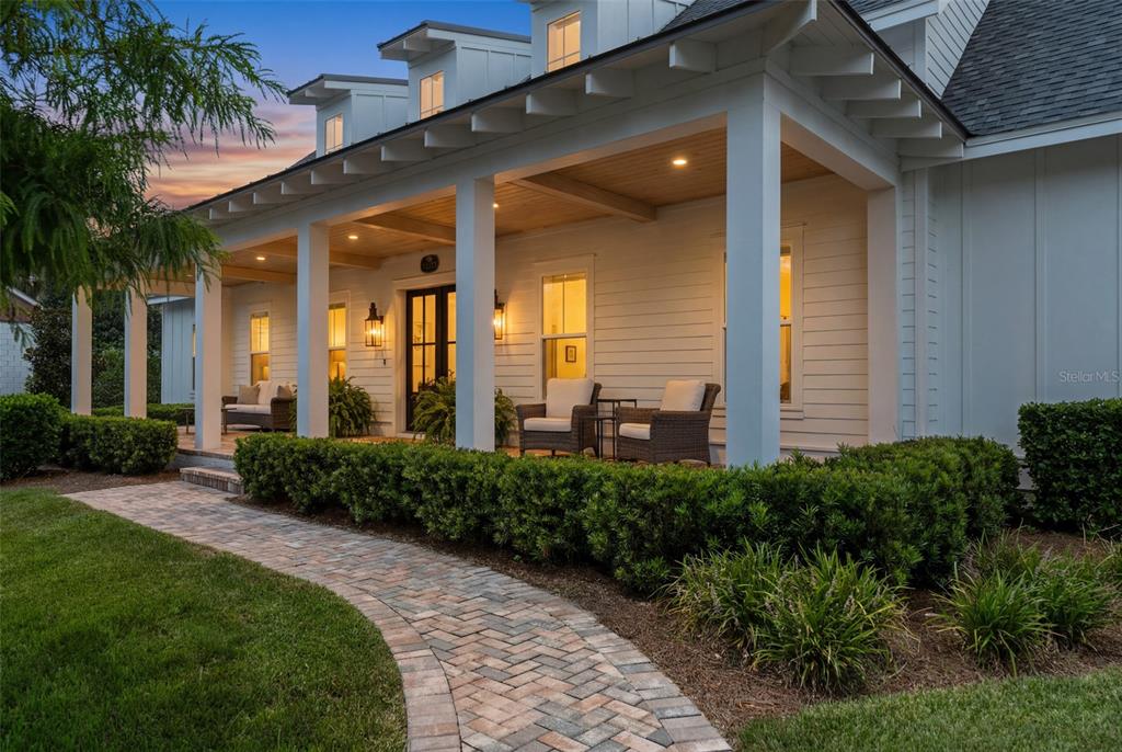 A white farmhouse with a covered porch, brick walkway, and manicured hedges at dusk — 15217 FARM STAND COURT, WINTER GARDEN, FL