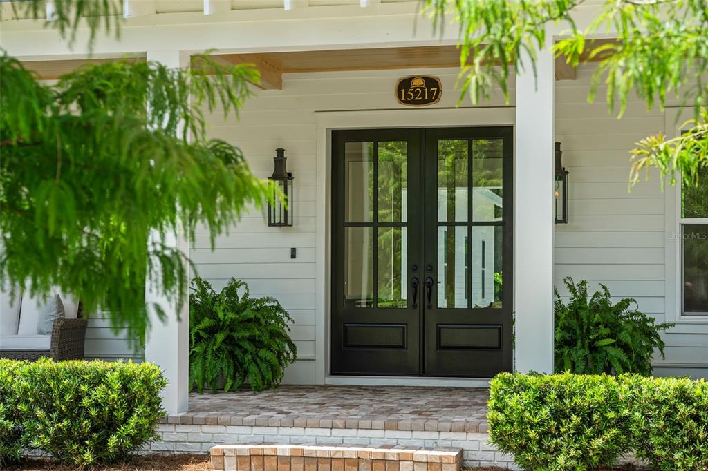 A front porch features a double glass door, white siding, and symmetrical lanterns — 15217 FARM STAND COURT, WINTER GARDEN, FL