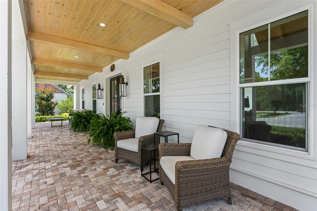 A covered porch features a wood-paneled ceiling, brick pavers, and two wicker chairs — 15217 FARM STAND COURT, WINTER GARDEN, FL
