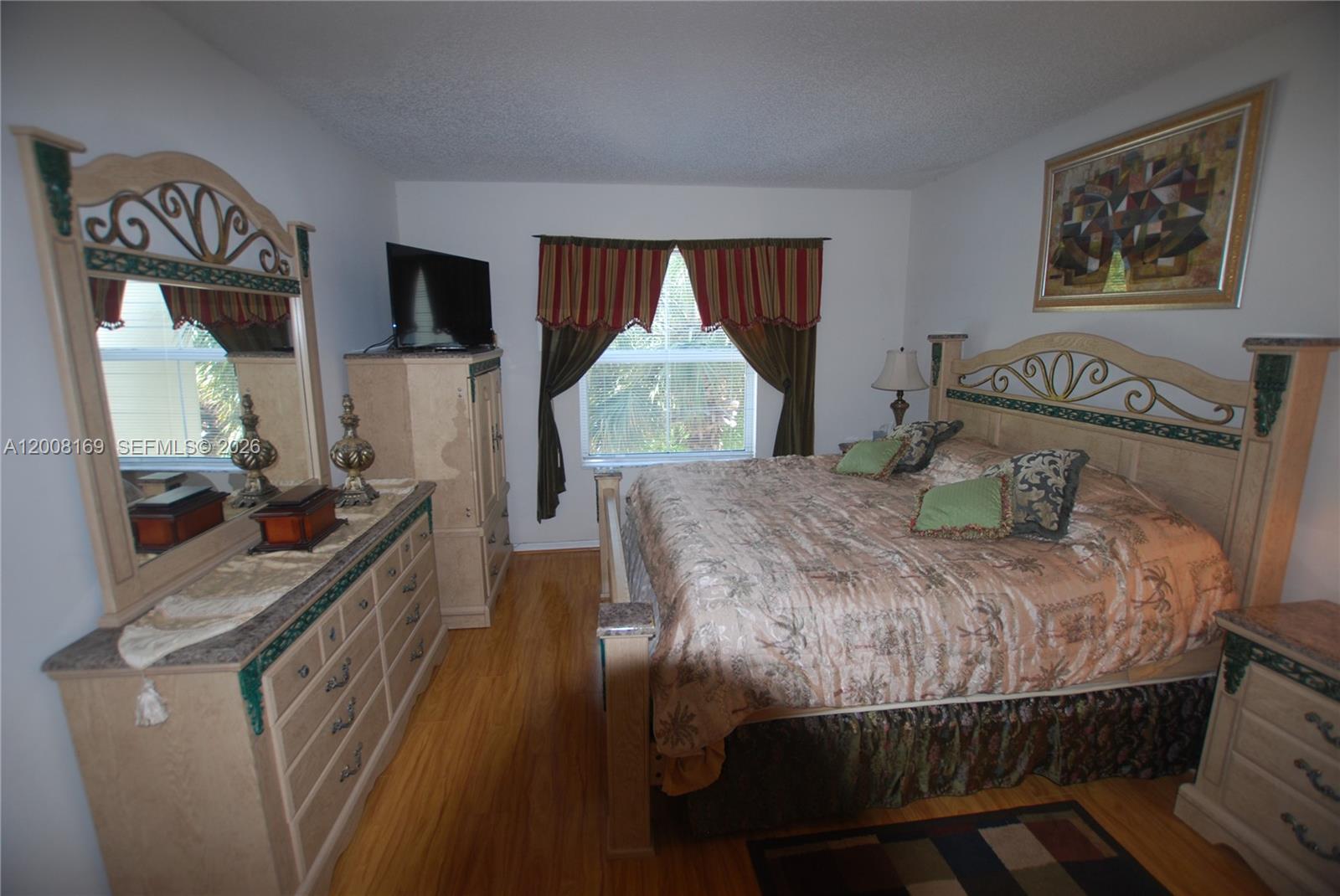 A bedroom features a wooden bed frame, matching dresser with mirror, and a window with curtains — 1310 Tuscany Way # 1310, Boynton Beach FL 33435, BOYNTON BEACH, FL