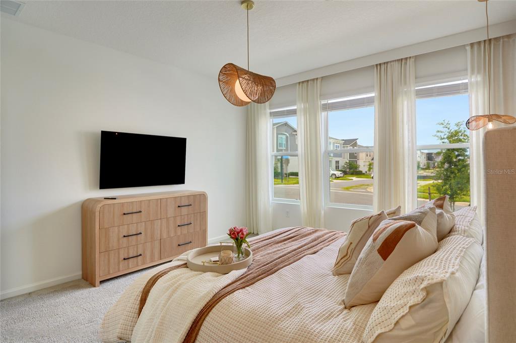 A bedroom features a light wood dresser, a mounted television, and a bed with neutral bedding — 9194 SEASCAPE COVE, KISSIMMEE, FL