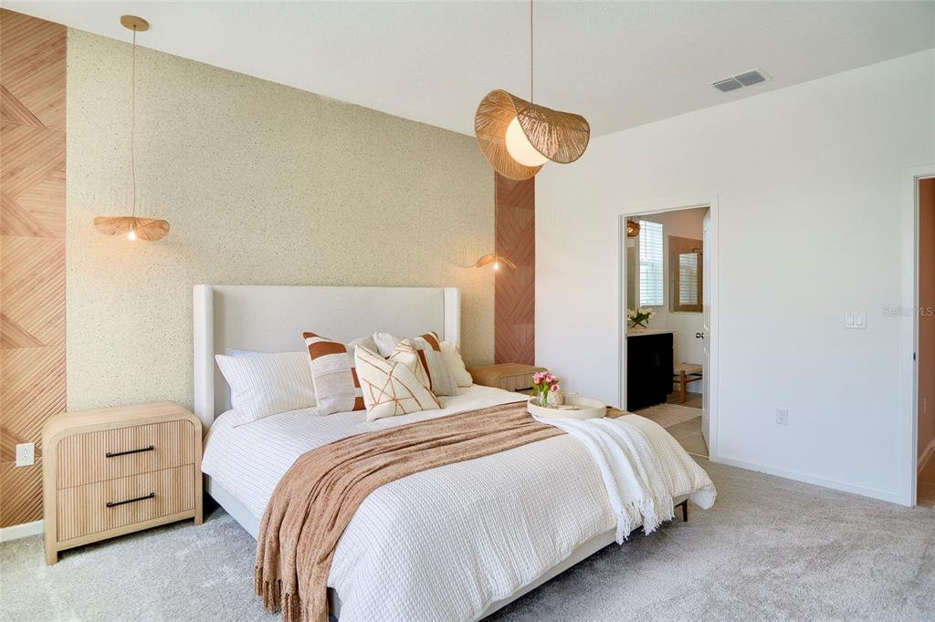 A bedroom features a textured accent wall, a bed with neutral bedding, and pendant lighting — 9194 SEASCAPE COVE, KISSIMMEE, FL