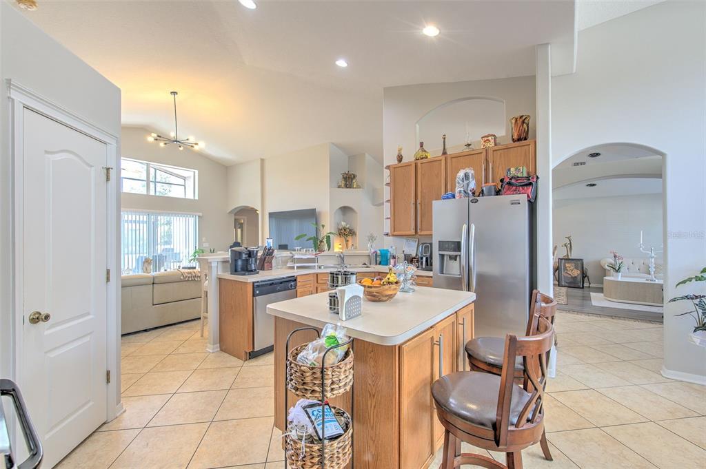 A kitchen with wood cabinets, a central island, and tile flooring opens to a living area — 4639 POINTE O WOODS DRIVE, WESLEY CHAPEL, FL
