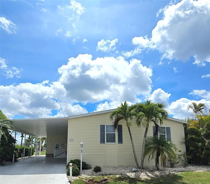 A single-story light yellow mobile home with a carport and palm trees under a blue sky — 29 BRINK AVENUE, PUNTA GORDA, FL