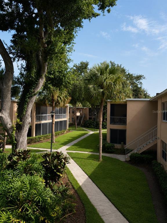 A sidewalk winds through a grassy courtyard between tan apartment buildings with palm trees — 4701 CHRISTA COURT UNIT 341, TAMPA, FL