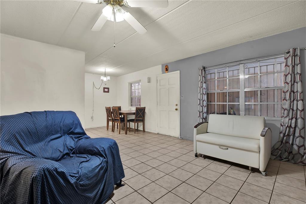A living room with tiled floors, a blue armchair, a white sofa, and a dining area — 4701 CHRISTA COURT UNIT 341, TAMPA, FL