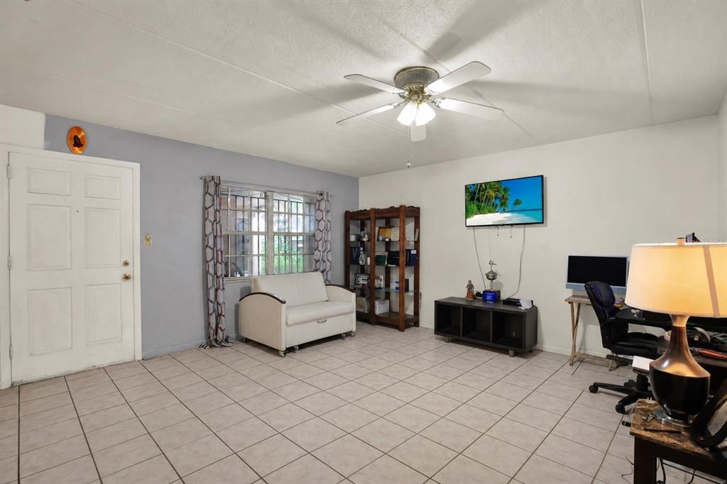 A living room with tiled floors, a white sofa, a television, and a computer desk — 4701 CHRISTA COURT UNIT 341, TAMPA, FL