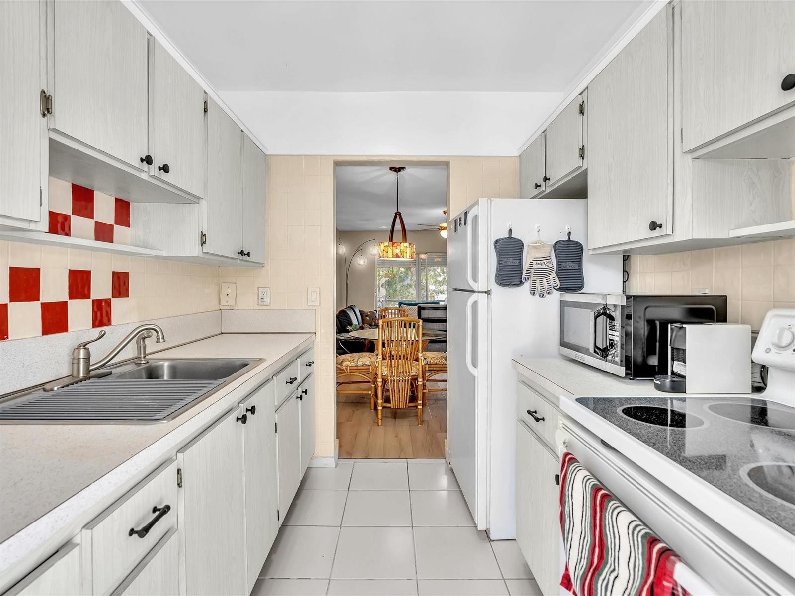 A galley kitchen features white cabinets, a stainless steel sink, and a red-and-white tiled backsplash — 2501 W Golf Boulevard # 234, Pompano Beach FL 33064, POMPANO BEACH, FL