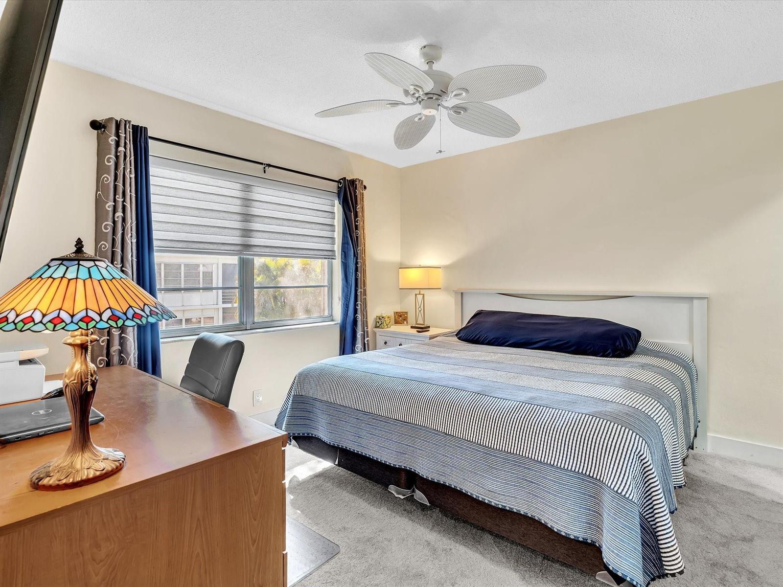 A bedroom features a bed with a striped quilt, a desk, and a ceiling fan — 2501 W Golf Boulevard # 234, Pompano Beach FL 33064, POMPANO BEACH, FL