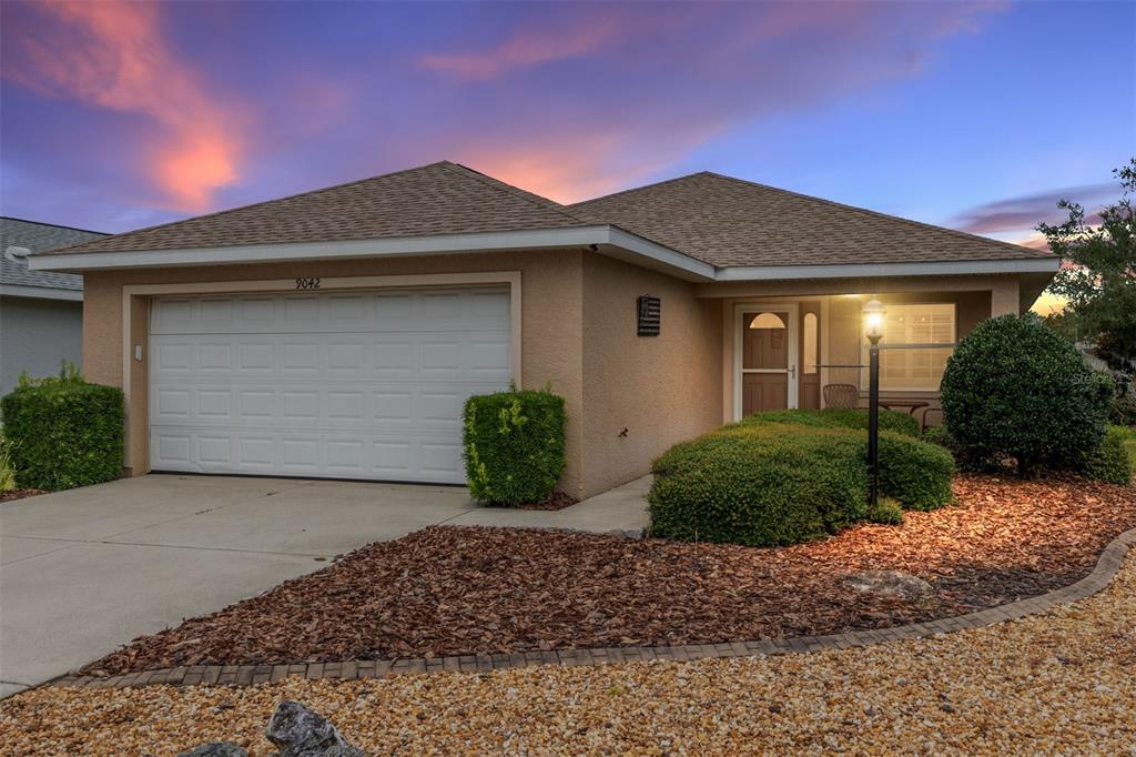 A single-story house with a tan stucco exterior, a two-car garage, and landscaped front yard — 9042 SW 102ND CIRCLE, OCALA, FL