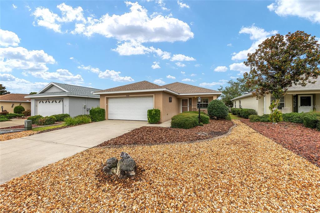 A single-story suburban house with a tan stucco exterior, a two-car garage, and gravel landscaping — 9042 SW 102ND CIRCLE, OCALA, FL