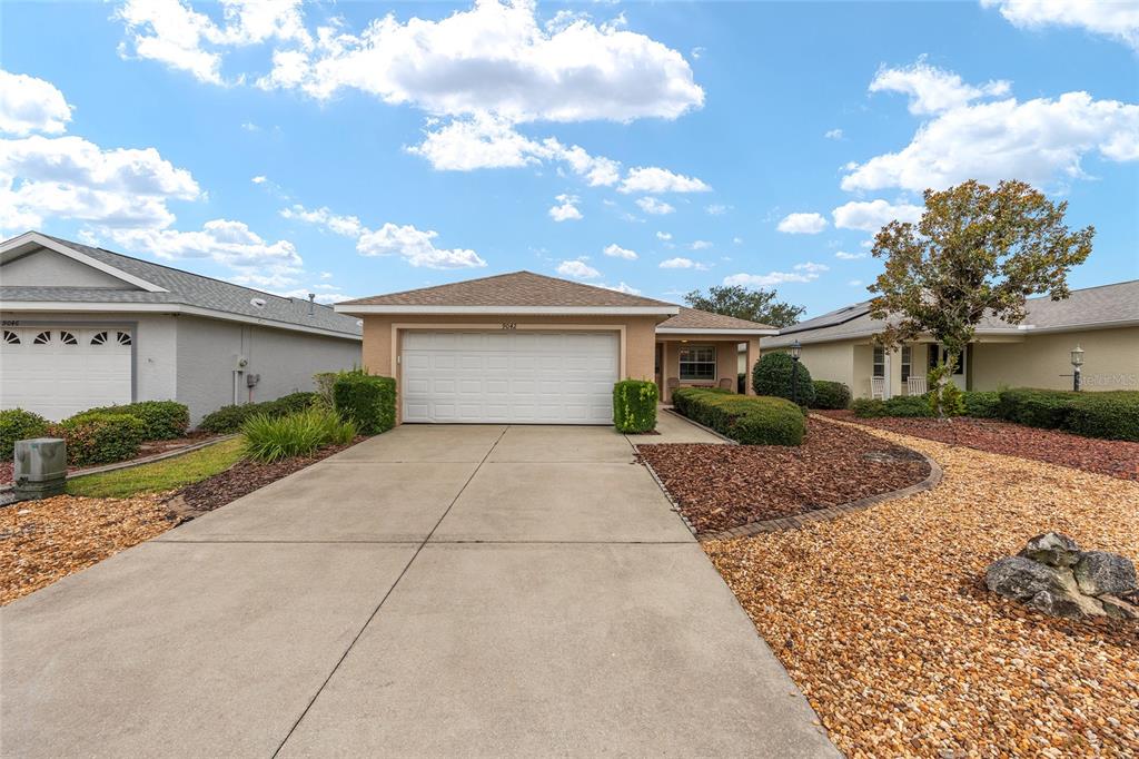 A single-story house with a white garage door, concrete driveway, and tan exterior — 9042 SW 102ND CIRCLE, OCALA, FL