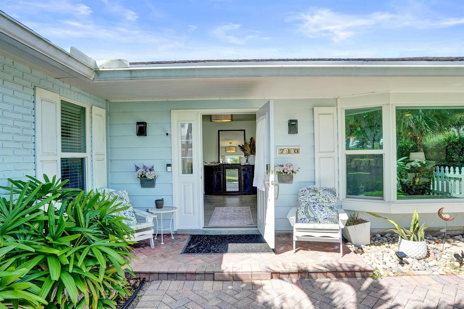 A light blue house exterior features a brick porch, two white chairs, and an open door — 710 NW 1st Avenue, Delray Beach FL 33444, DELRAY BEACH, FL