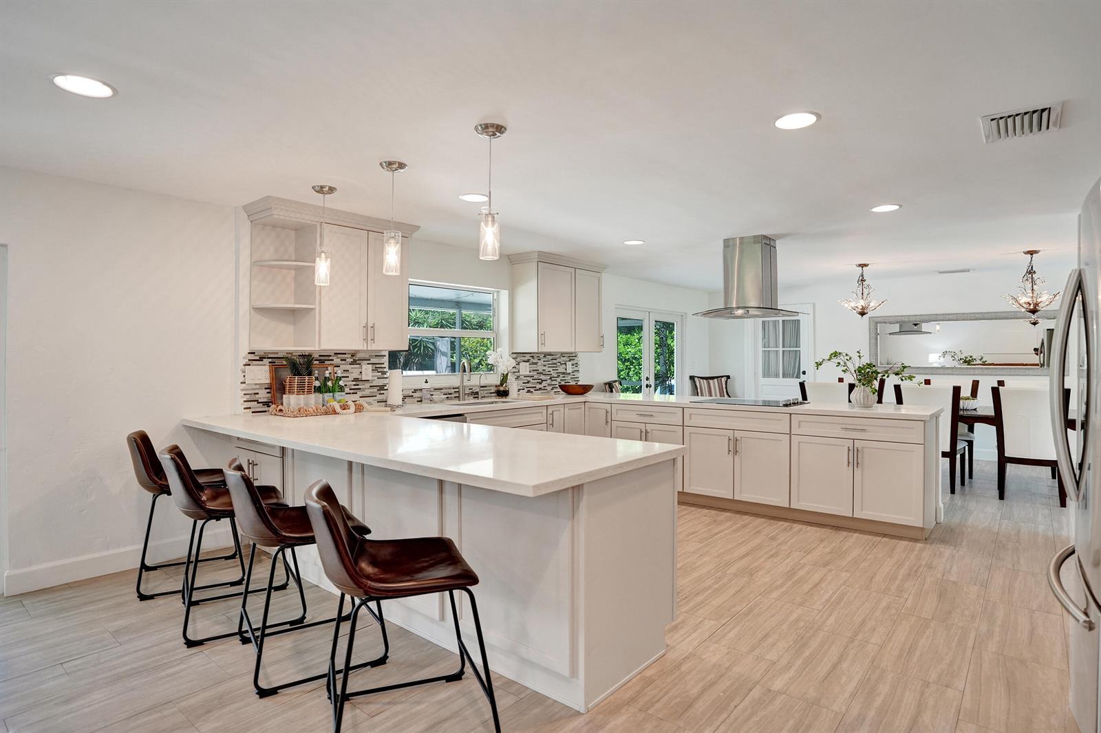 A modern kitchen features white cabinetry, a large island with bar seating, and light flooring — 710 NW 1st Avenue, Delray Beach FL 33444, DELRAY BEACH, FL