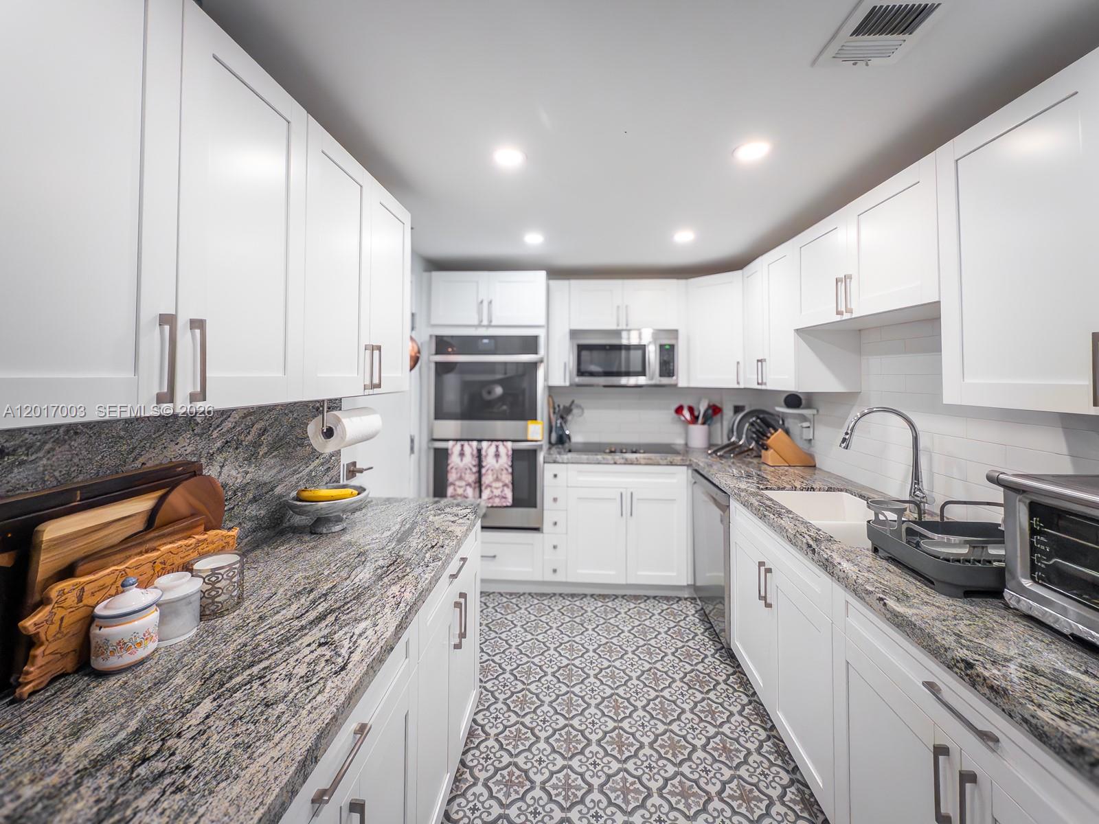A kitchen features white cabinetry, granite countertops, and patterned tile flooring — 90 Edgewater Dr # 114, Coral Gables FL 33133, CORAL GABLES, FL