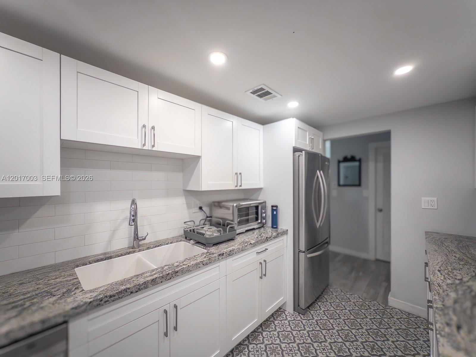 A kitchen features white cabinets, granite countertops, a double sink, and patterned tile flooring — 90 Edgewater Dr # 114, Coral Gables FL 33133, CORAL GABLES, FL