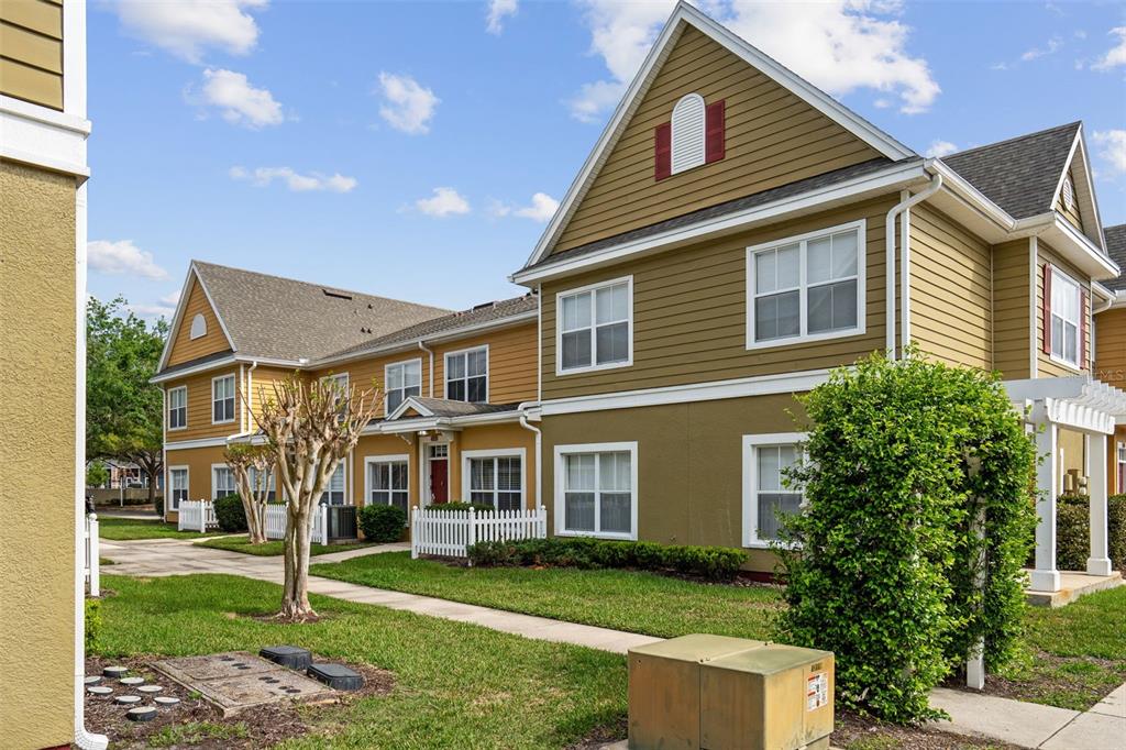 A multi-story tan and yellow townhouse exterior with white trim, windows, and a small lawn — 4561 YELLOWGOLD ROAD E UNIT 103, KISSIMMEE, FL