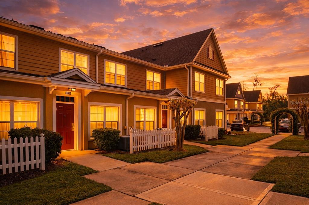 A multi-story townhouse exterior with a red door, white picket fence, and sunset sky — 4561 YELLOWGOLD ROAD E UNIT 103, KISSIMMEE, FL