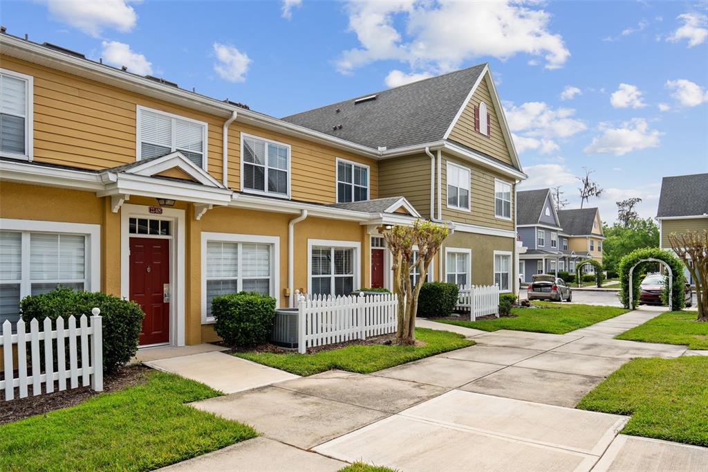 A two-story yellow townhouse with a white picket fence and a red front door — 4561 YELLOWGOLD ROAD E UNIT 103, KISSIMMEE, FL