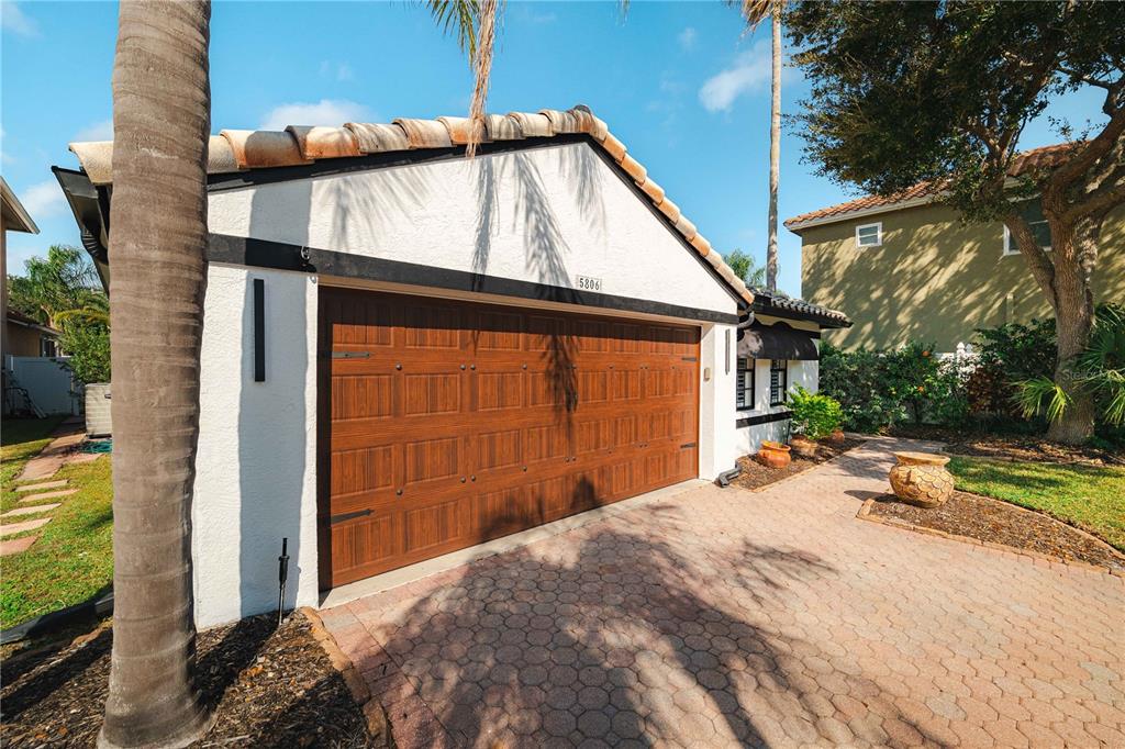 A white garage with a wood-look door and a tiled roof sits beside a driveway — 5806 CAY COVE COURT, TAMPA, FL