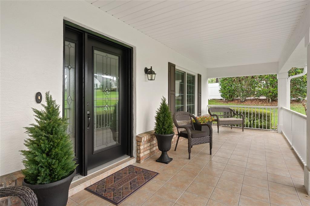 A covered front porch features tiled flooring, a black front door, and wicker seating — 5402 NW 76TH COURT, OCALA, FL