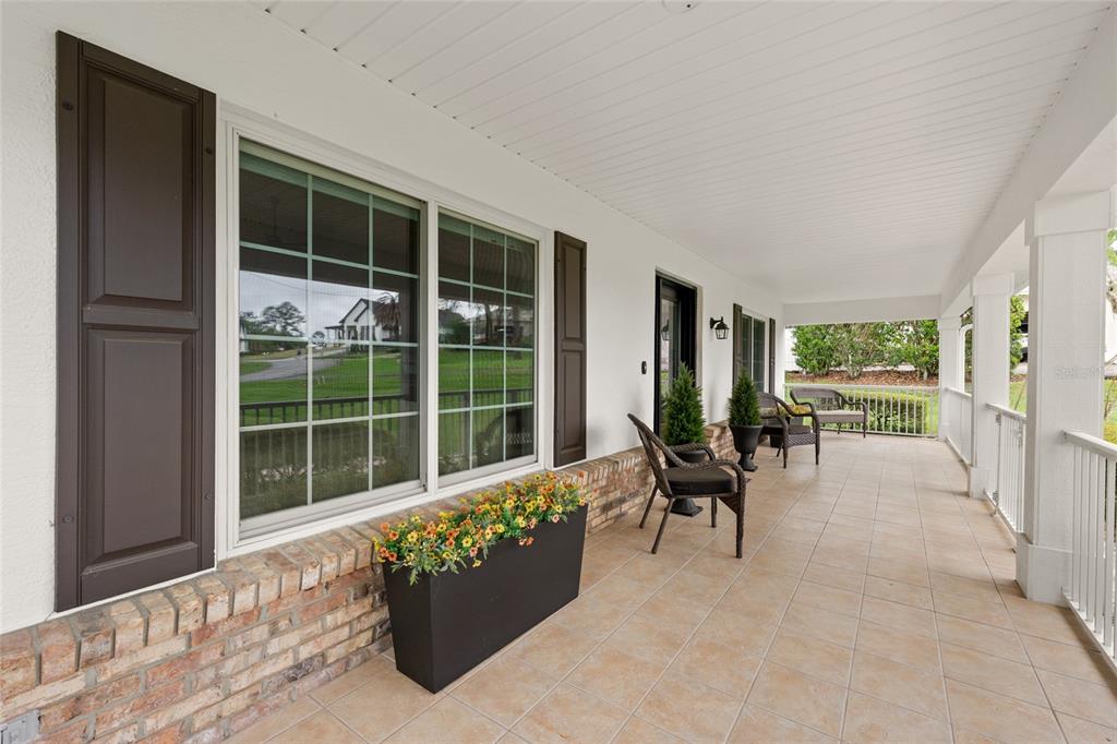 A covered porch features tiled flooring, brick accents, a large window with shutters, and seating — 5402 NW 76TH COURT, OCALA, FL